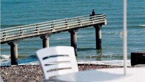 A beach with a pier extending into the water, white lounge chairs, and a white umbrella. - Du Casino (Vierville-sur-Mer)