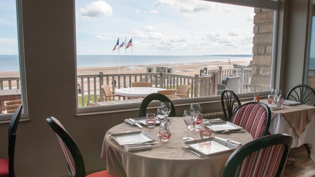 A dining area with a table set for four, overlooking a beach with flags. - Du Casino (Vierville-sur-Mer)