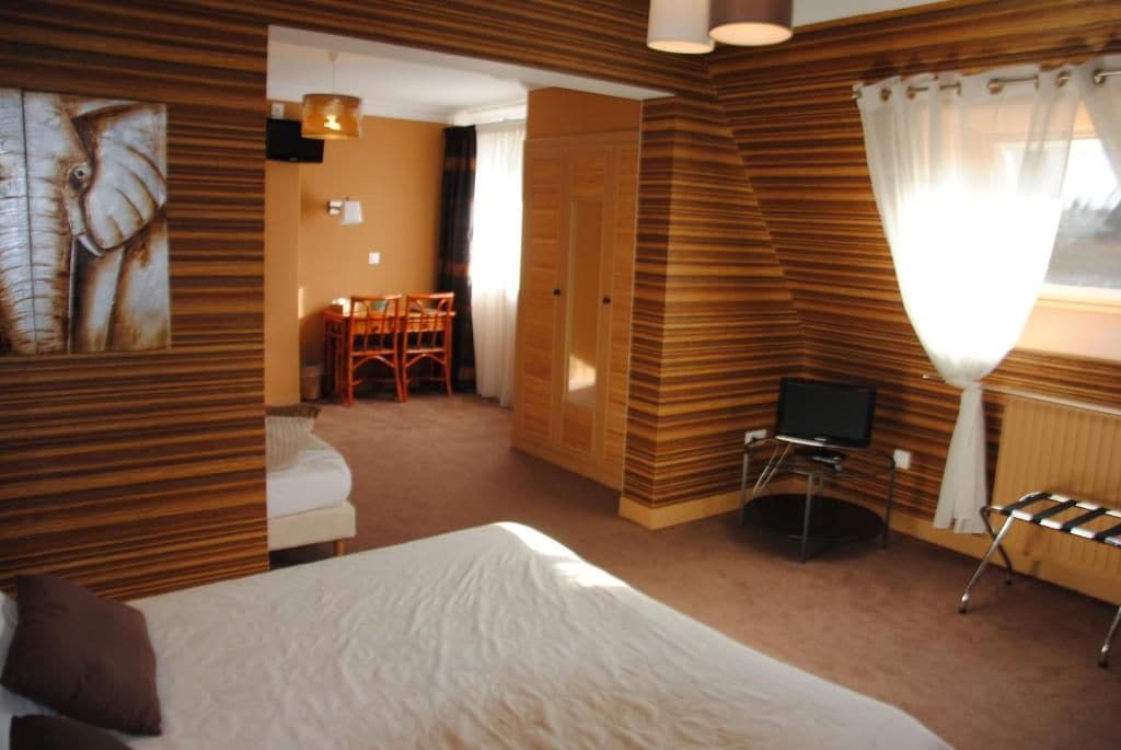 A hotel room with a bed, a television, a seating area with chairs, and a wooden wall design.