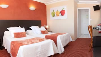 A hotel room with two beds, a desk, and a chair. There is a painting of apples on the wall and a red curtain on the left.