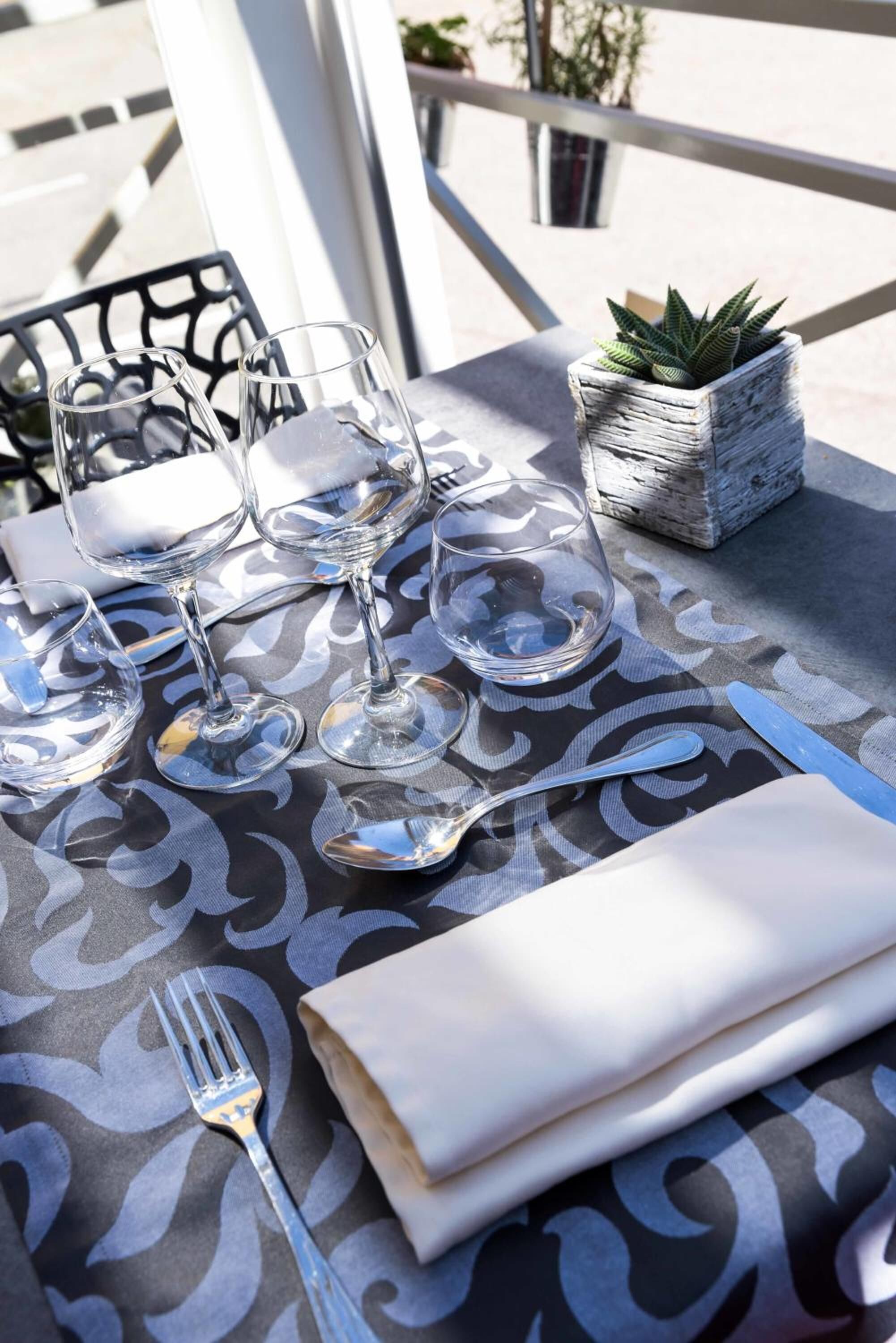 A table set with wine glasses, a fork, a knife, and a napkin, with a small potted plant on the table.
