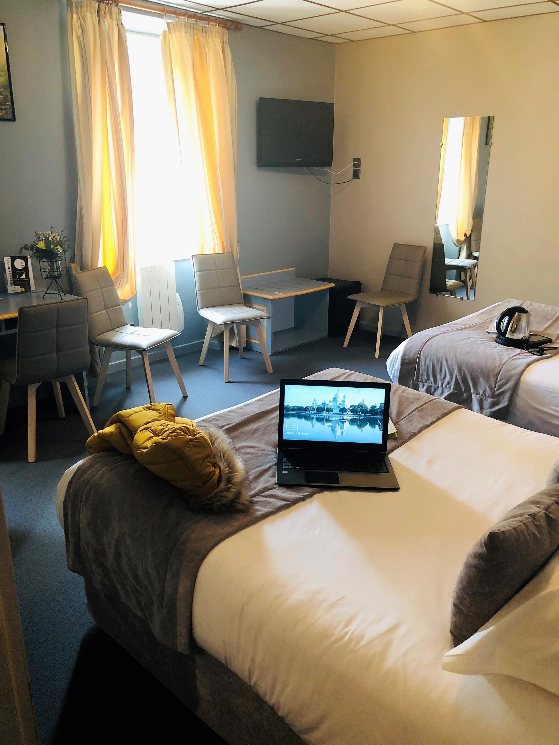 A hotel room with two beds, a desk, a chair, a television, and a laptop.