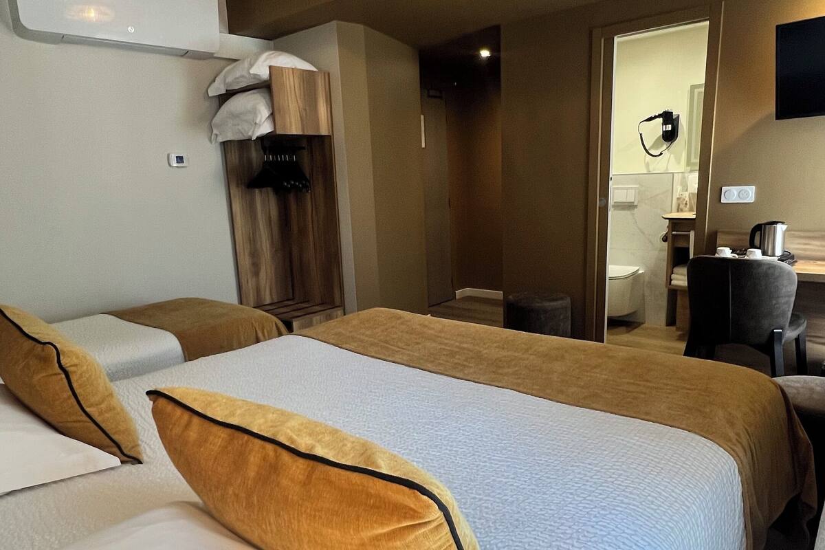 A hotel room with two beds, a desk, a chair, a wardrobe, and a bathroom visible through an open door.