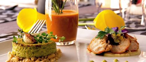 Un plato con un mousse verde, un vaso de líquido rojo con un adorno, y una fruta amarilla sobre un plato blanco.