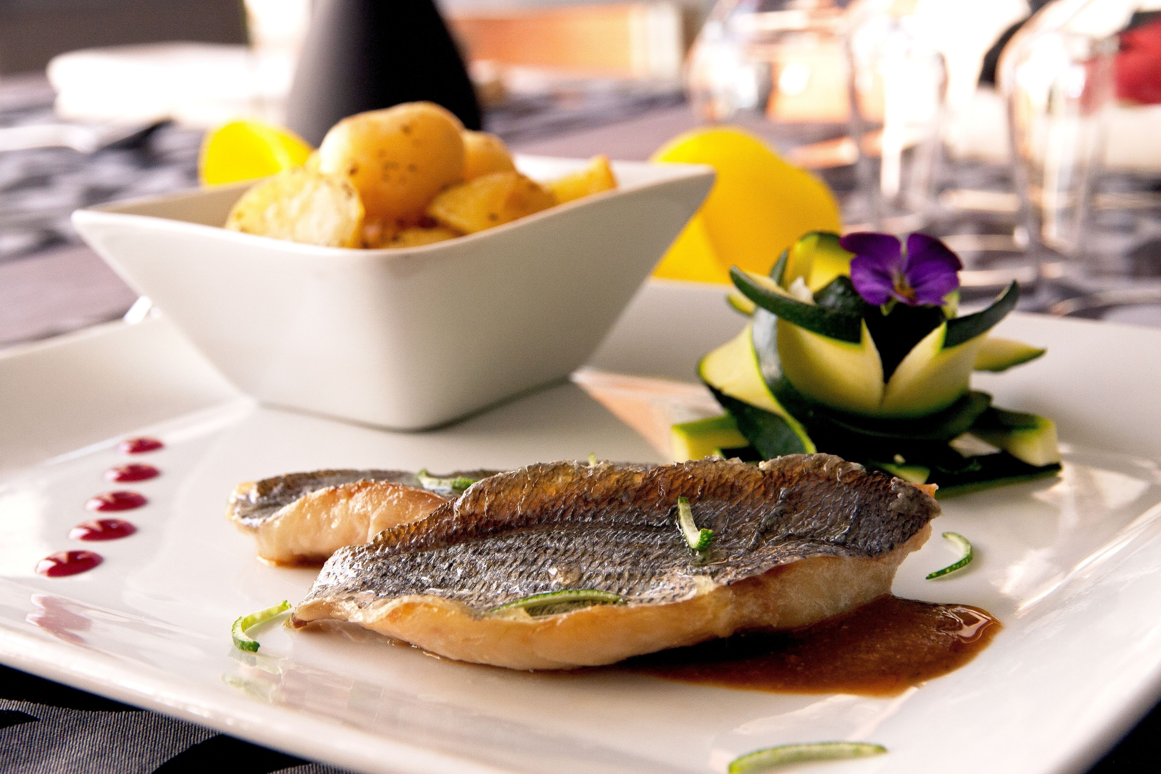 Ein Teller mit Fisch, Zitronenscheiben und einer kleinen Schüssel Kartoffeln.