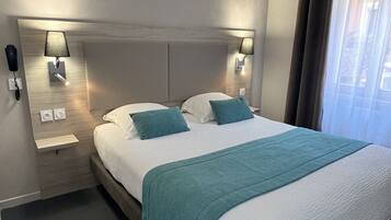 Una habitación de hotel moderna con una cama grande, dos mesitas de noche con lámparas, un ventilador de techo y una ventana con cortinas.