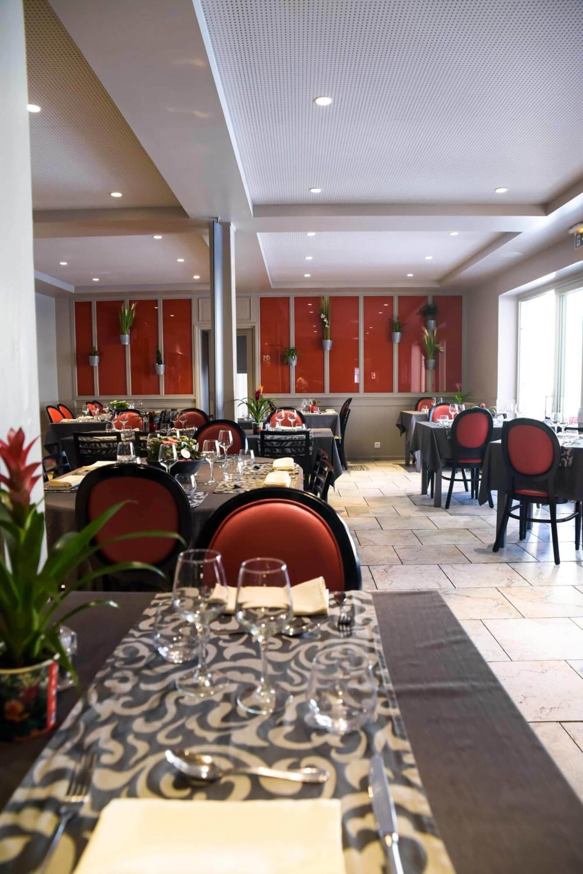 A dining area with tables set for multiple people, chairs, and potted plants.