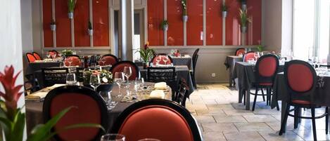 A dining area with tables set for multiple people, chairs, and potted plants.