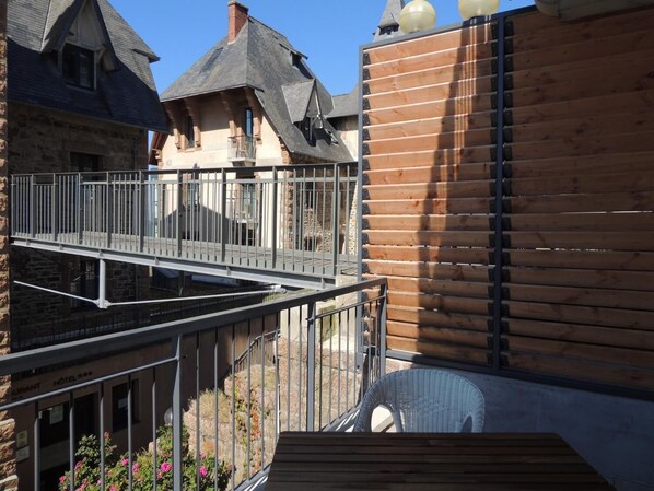 Un hotel con fachada de madera, un balcón con barandilla de metal y un edificio de piedra al fondo.