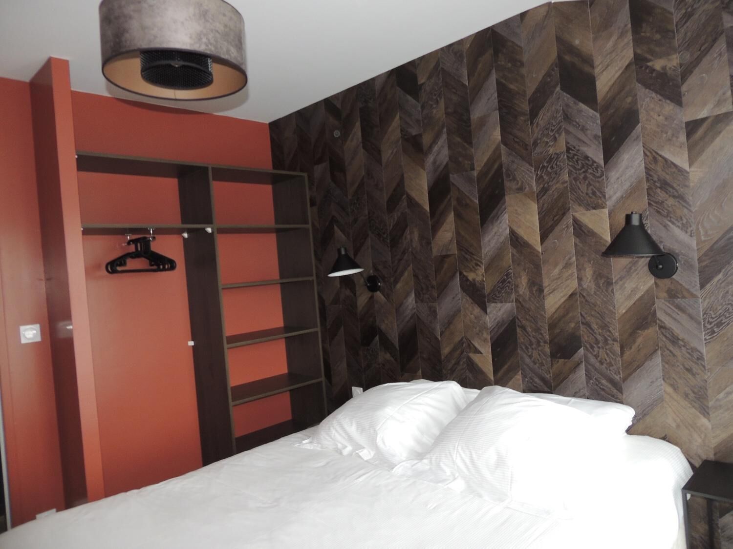A bedroom with a bed, a wardrobe, and a wall with a herringbone pattern.