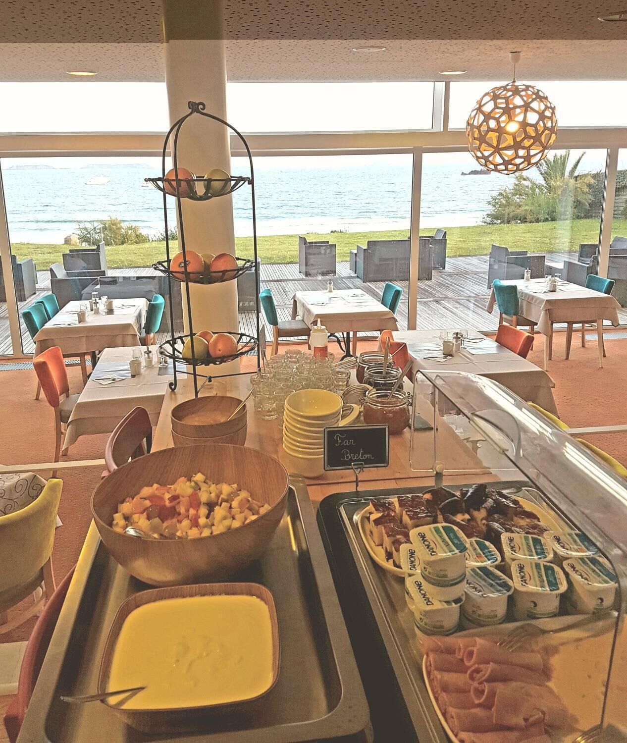 A buffet area with a view of the sea, featuring a variety of food items and a sign indicating 'Pan Breton'.