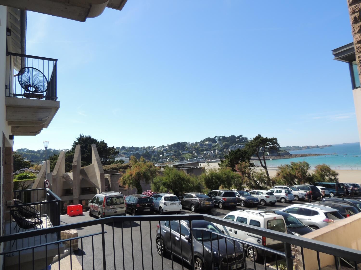 A parking lot with several cars, a view of a beach, and buildings in the background.