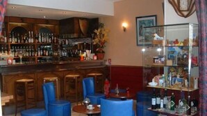 A bar area with wooden cabinets, blue bar stools, and a glass display case with various items. - Bel'Air (Jausiers)