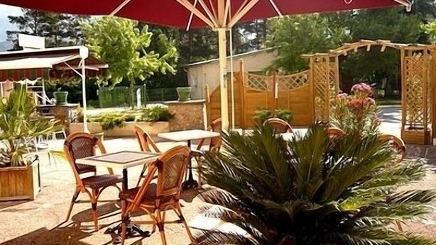 An outdoor patio with wooden chairs and tables, a red umbrella, and a decorative wooden archway. - Bel'Air (Jausiers)