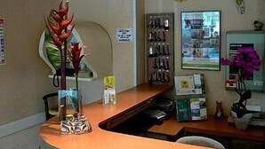 A reception desk with a vase of red flowers, a bulletin board with various notices, and a wall-mounted decorative item.
