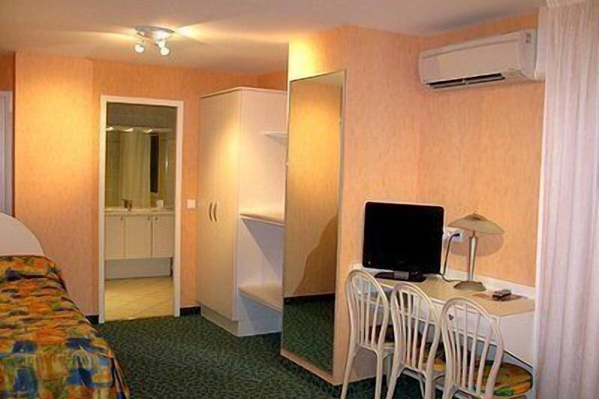 Una habitación de hotel con cama, escritorio, silla, televisión y aire acondicionado.