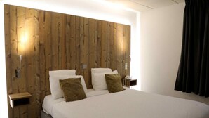 Camera d'albergo con testiera in legno, letto con biancheria bianca e due cuscini, comodino con lampada e telefono.