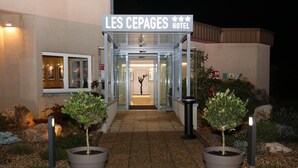 L'ingresso dell'Hotel Les Cepages, con una porta vetrata, piante in vaso e un vialetto ben illuminato.
