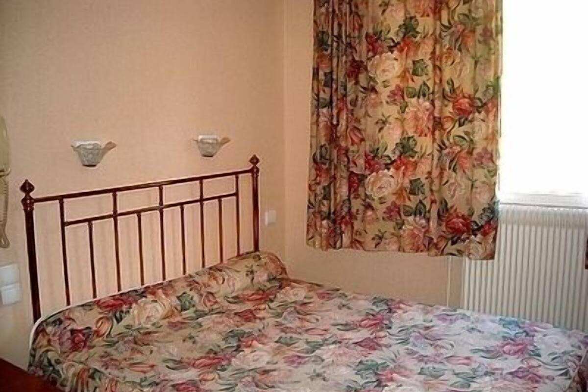 A bedroom with a floral bedspread, a wooden headboard, and a window with a floral curtain.