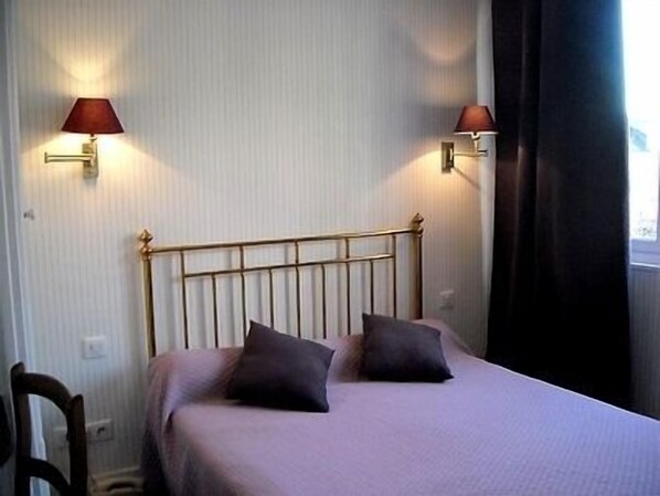 A single bed with a metal frame and two pillows, flanked by two wall-mounted lamps with red shades, in a room with vertical striped wallpaper.