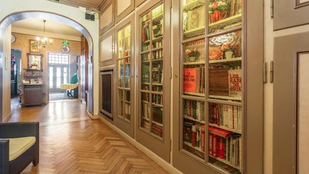 A hallway with a herringbone floor, a wicker chair, and a bookshelf filled with books and decorative items. - Remotel (Knutange)