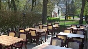 An outdoor seating area with multiple tables and chairs, surrounded by trees and a fence. - Remotel (Knutange)