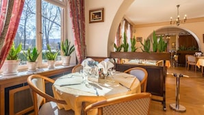 A dining area with a table set for two, potted plants, and a view through the window. - Remotel (Knutange)