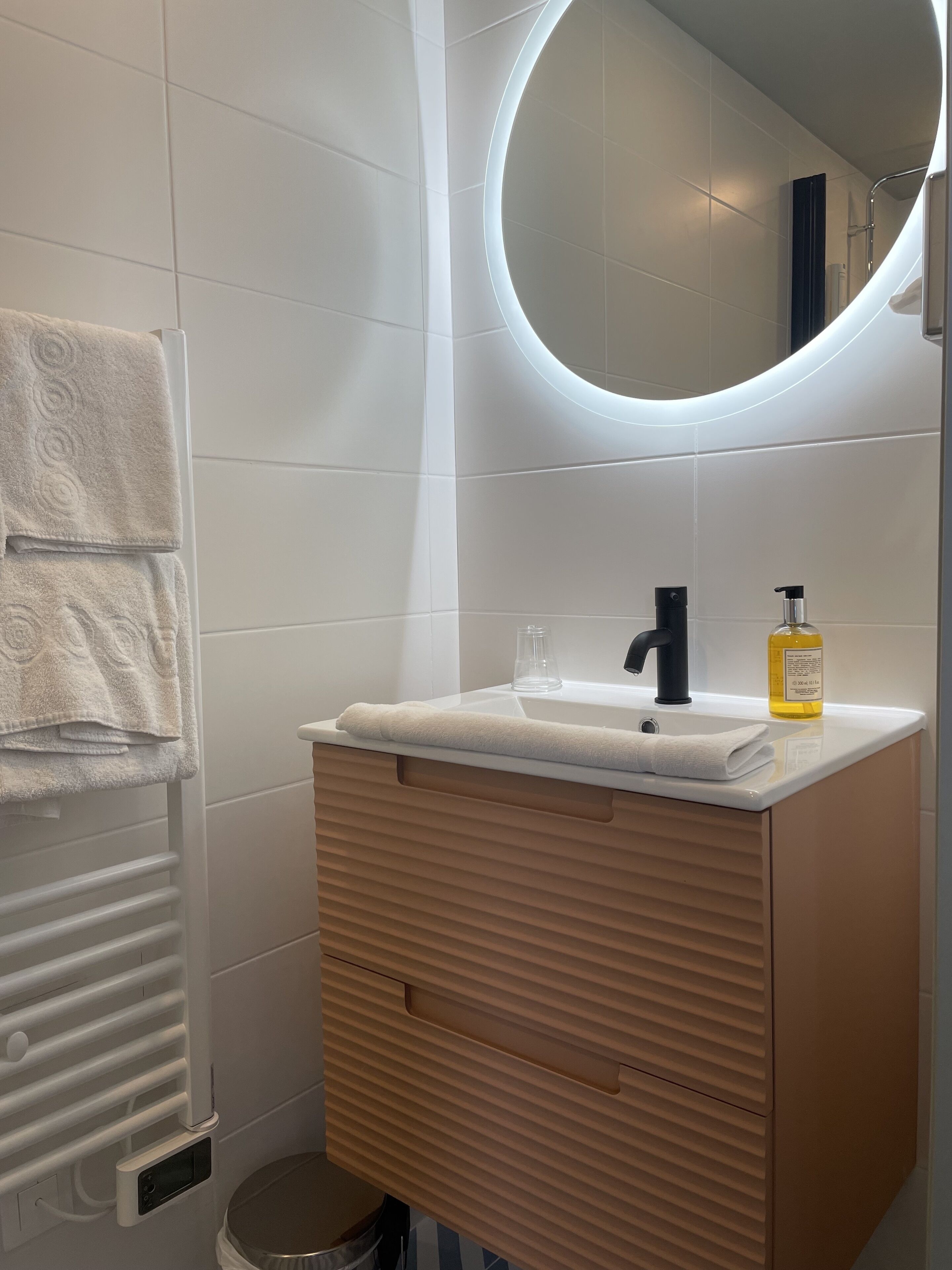 Un baño moderno con tocador blanco, espejo redondo y perchero.