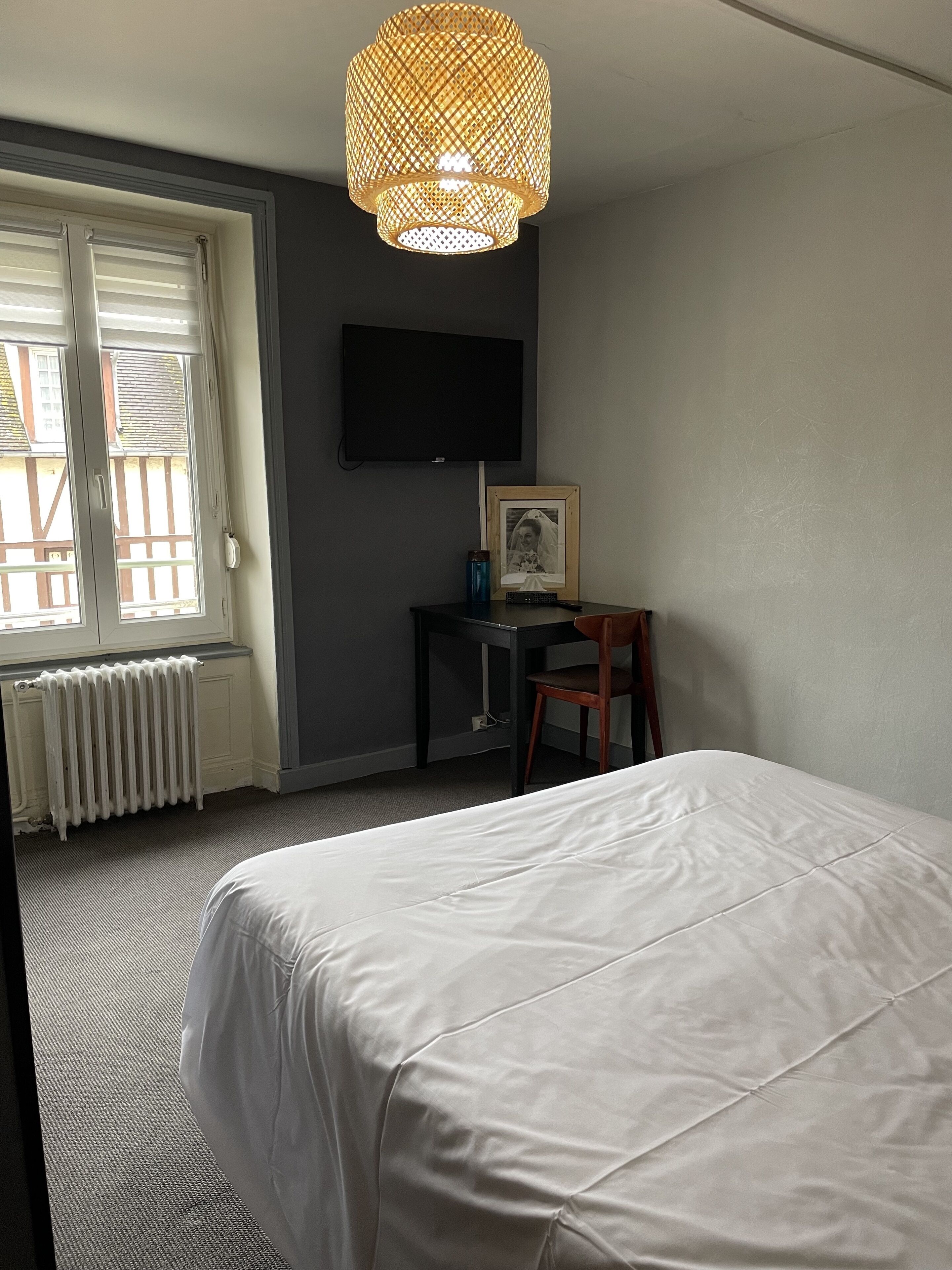 Een slaapkamer met een bed, een bureau met stoel, een televisie en een raam met jaloezieën.