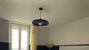 Ein ordentlich bezogenes Bett mit weißen Leinen, einer Nachttischlampe und einem Fenster mit Vorhängen.