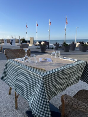 An outdoor dining area with a checkered tablecloth, wicker chairs, and flags.