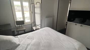 A hotel room with a large bed, a desk, a chair, a radiator, and a window with blinds.