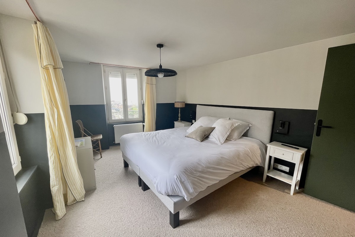 A neatly arranged bedroom with a large bed, bedside tables, a window with curtains, and a hanging light fixture.
