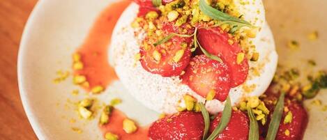Un postre con base blanca, cubierto de fruta roja y hojas verdes, decorado con elementos amarillos y verdes, sobre un plato blanco.
