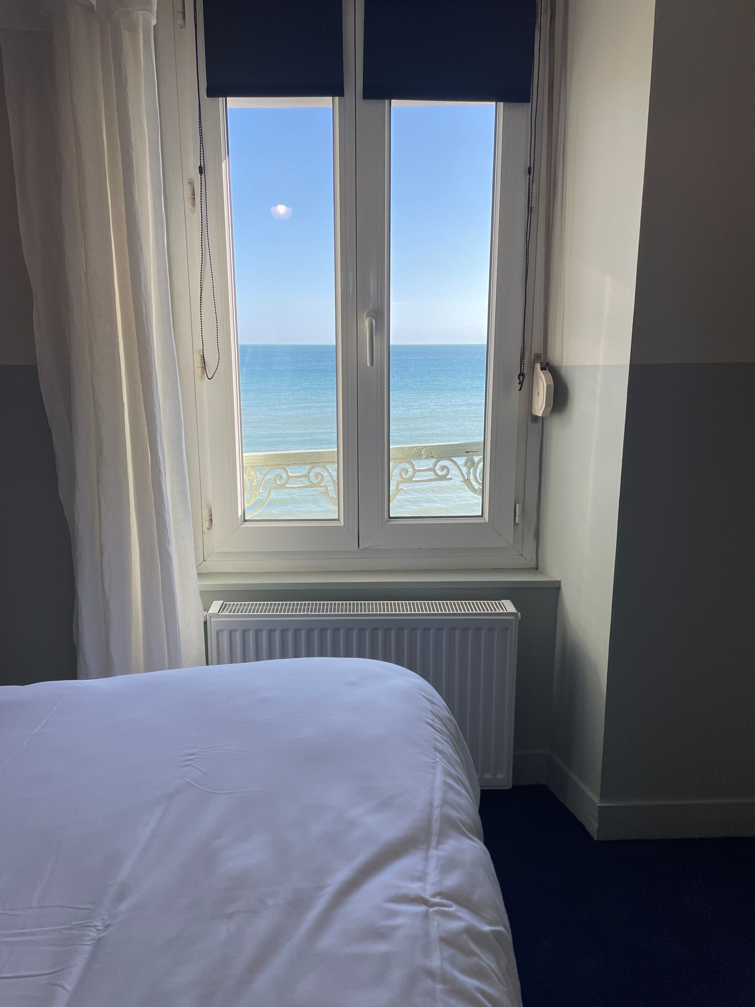 A hotel room with a bed, a window with a view of the sea, and a radiator below the window.