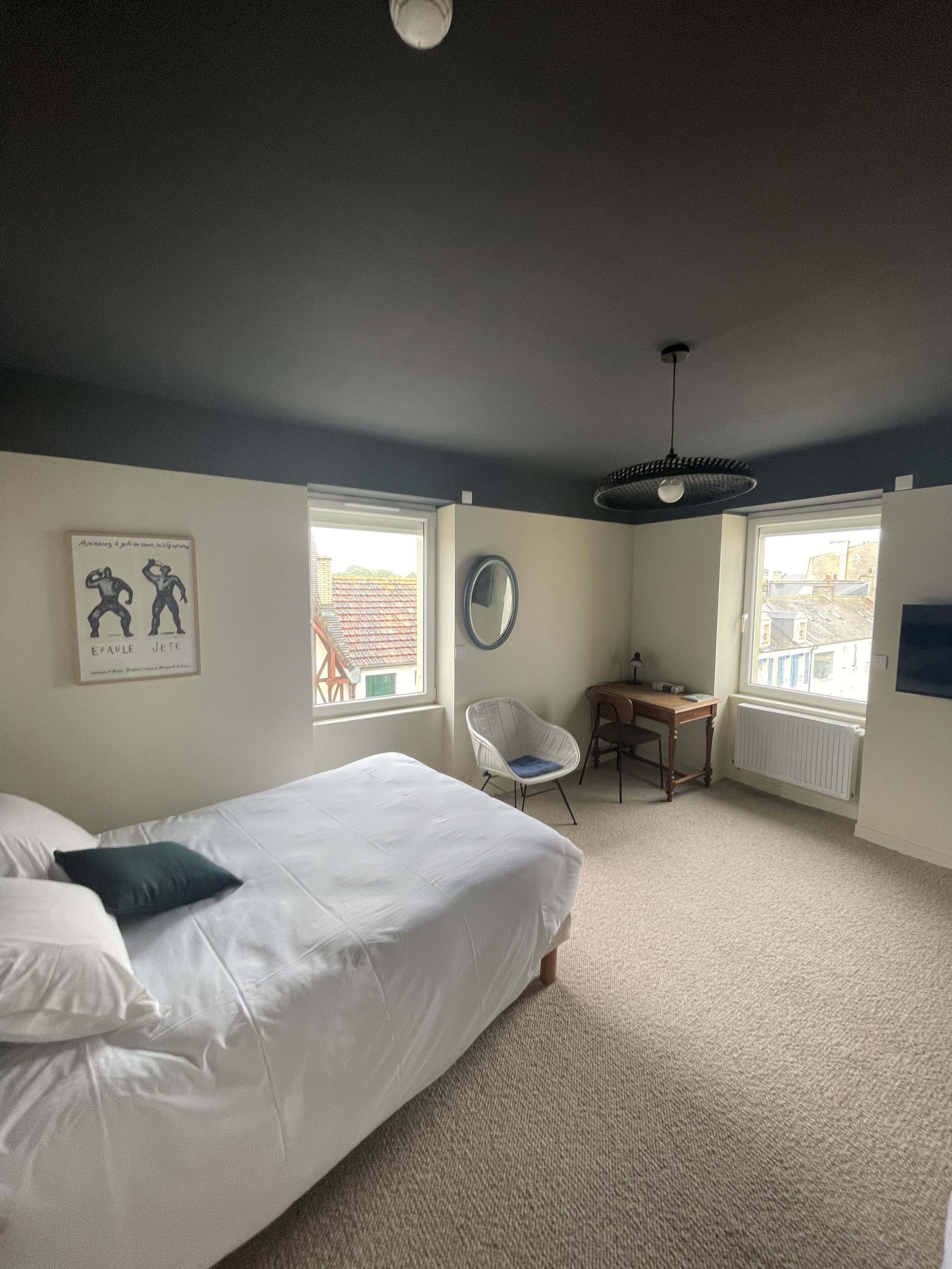 A bedroom with a bed, a chair, a desk, a mirror, and windows.