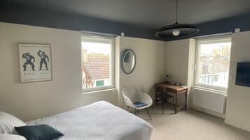 A bedroom with a bed, a chair, a desk, a mirror, and windows.