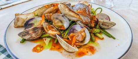 A seafood dish on a plate with clams, asparagus, and a piece of fish, served on a table with a checkered tablecloth.