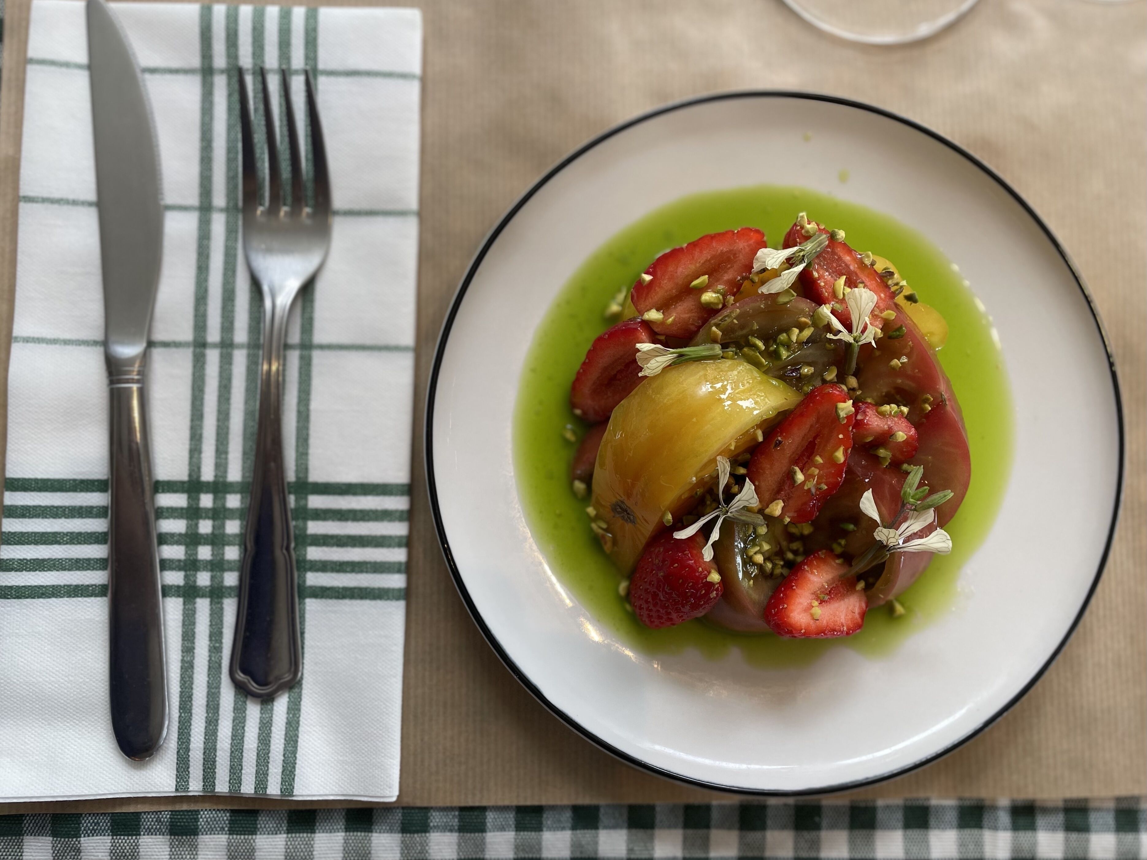 A plate of food with a green sauce, strawberries, and a yellow fruit, served on a white plate with a black rim.