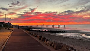 A coastal walkway with a pier extending into the sea, featuring a rocky breakwater and street lamps. - Le Beau Rivage (Luc-sur-Mer)