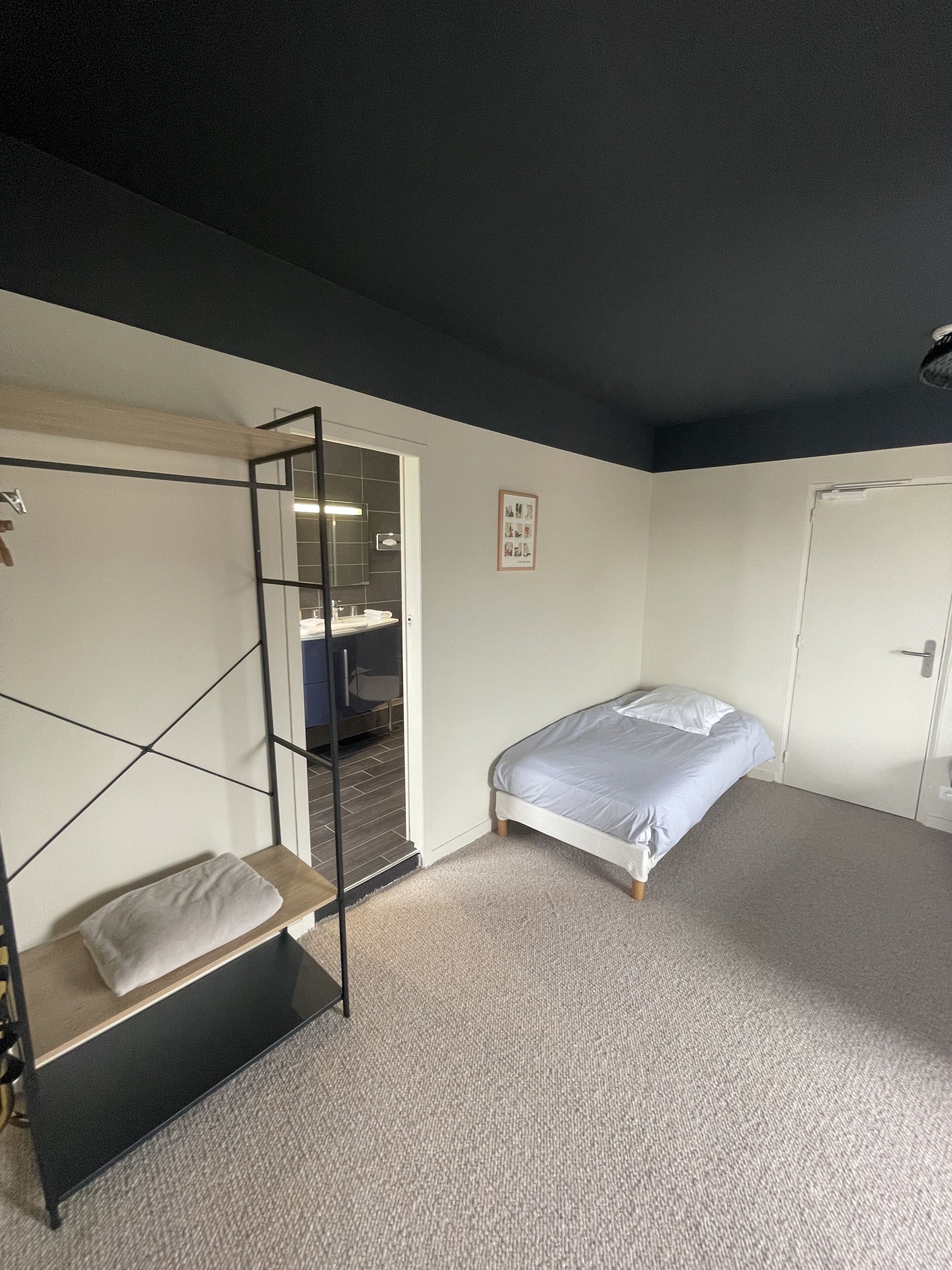 Une chambre avec un lit superposé, un lit simple, une porte et un tableau encadré au mur.