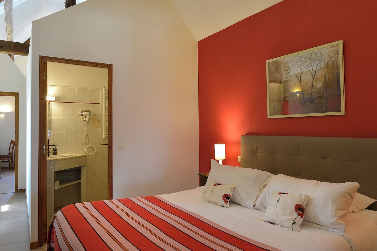 A hotel room with a bed, a painting on the wall, and a bathroom visible through an open door.