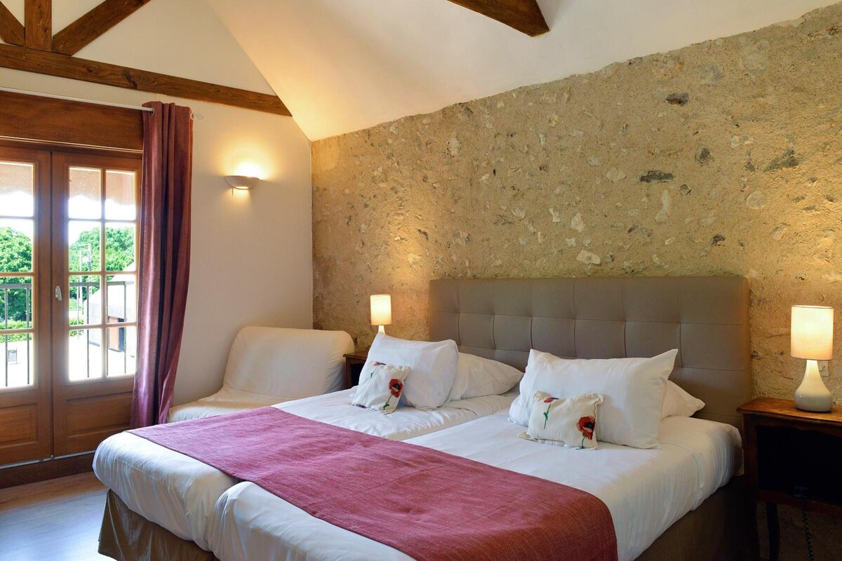 A double bed with a headboard, two bedside lamps, and a view of the outdoors through a door with curtains.