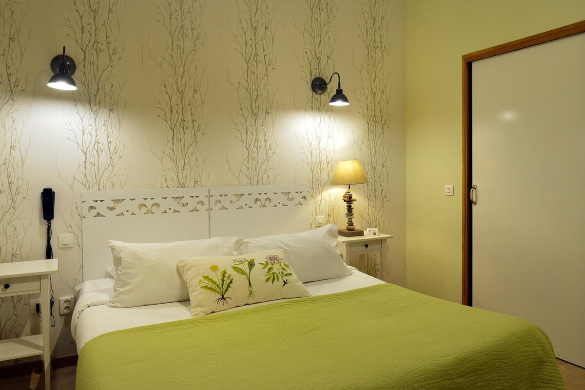 A bedroom with a bed, two bedside lamps, a nightstand, a wall-mounted telephone, and a door.