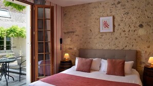 A bedroom with a large bed, two bedside lamps, a wooden headboard, and a window with a view of greenery outside. - Auberge Le Colombien - Hôtel Restaurant (Villandry)