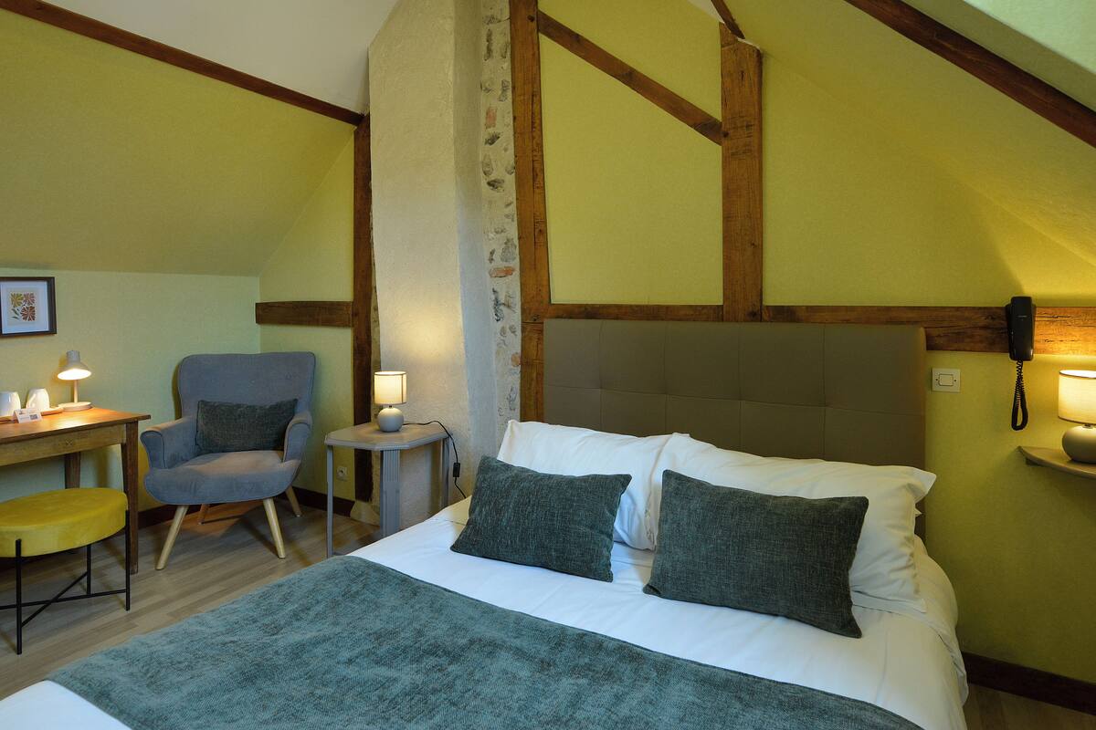 A hotel room with a bed, a chair, a desk, and a phone on the wall.