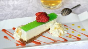 Una rebanada de pastel de queso con fresa encima, rociada con salsa roja y amarilla, sobre un plato blanco.
