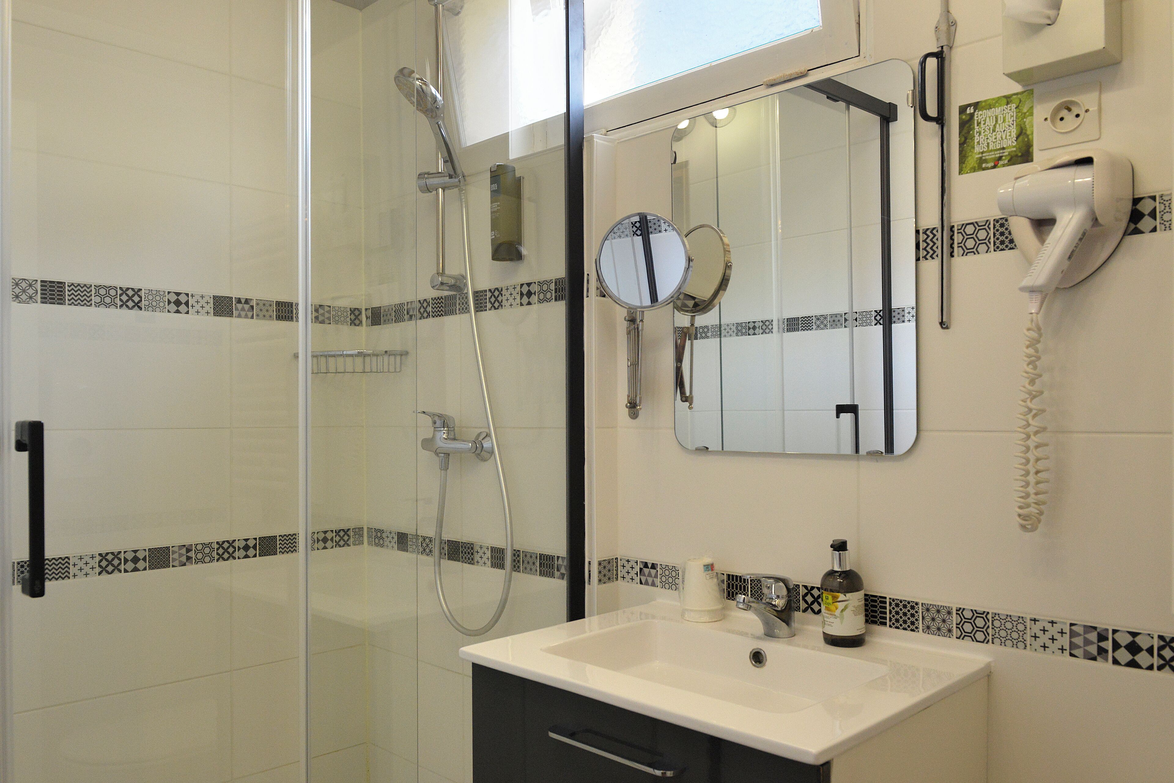 Un baño con cabina de ducha de vidrio, un lavamanos blanco con espejo y un secador de pelo montado en la pared.
