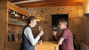 Two people standing at a wooden bar with shelves of bottles and glasses. - Auberge Le Colombien - Hôtel Restaurant (Villandry)