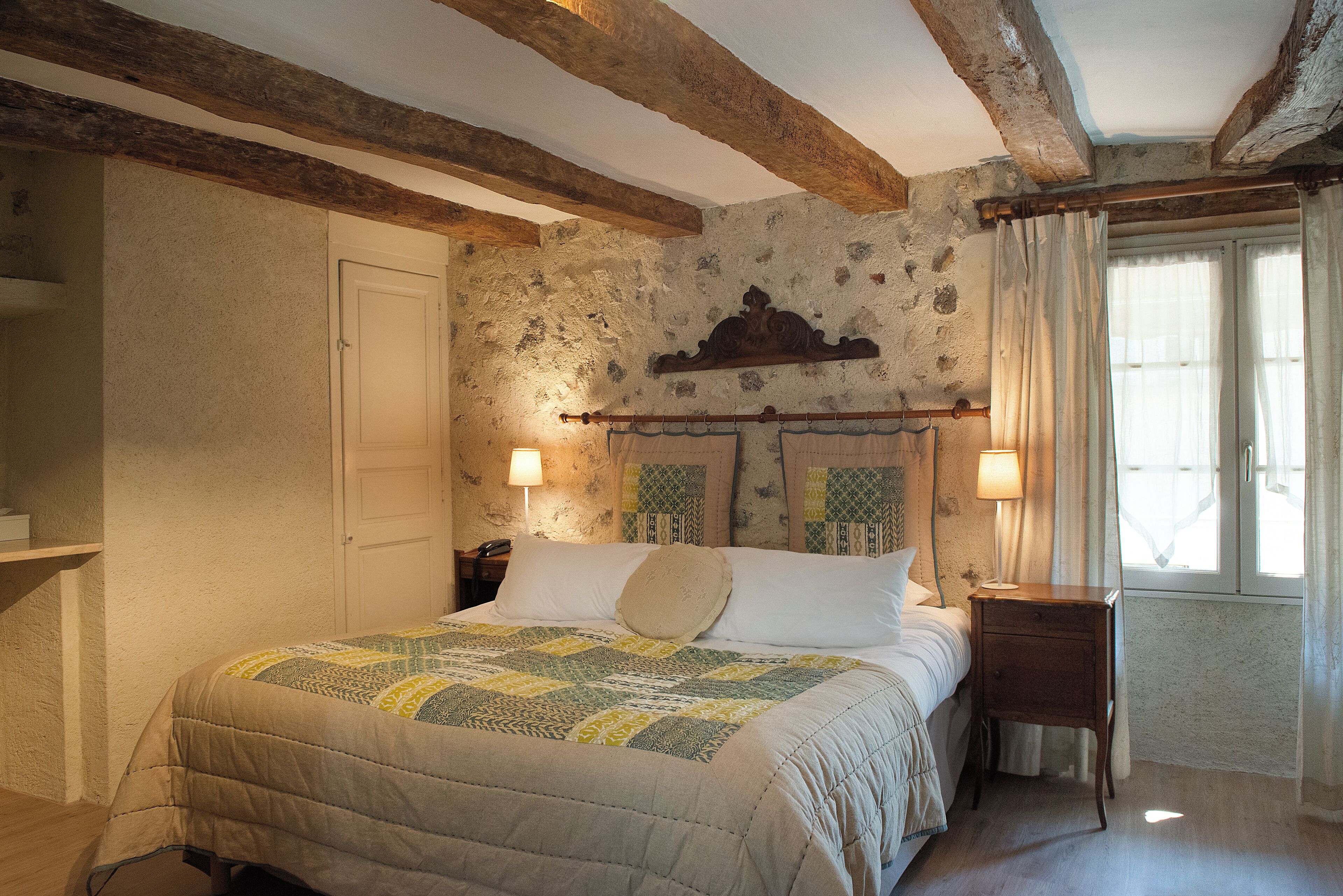 Un dormitorio con cama, mesita de noche, lámpara y pared de piedra.